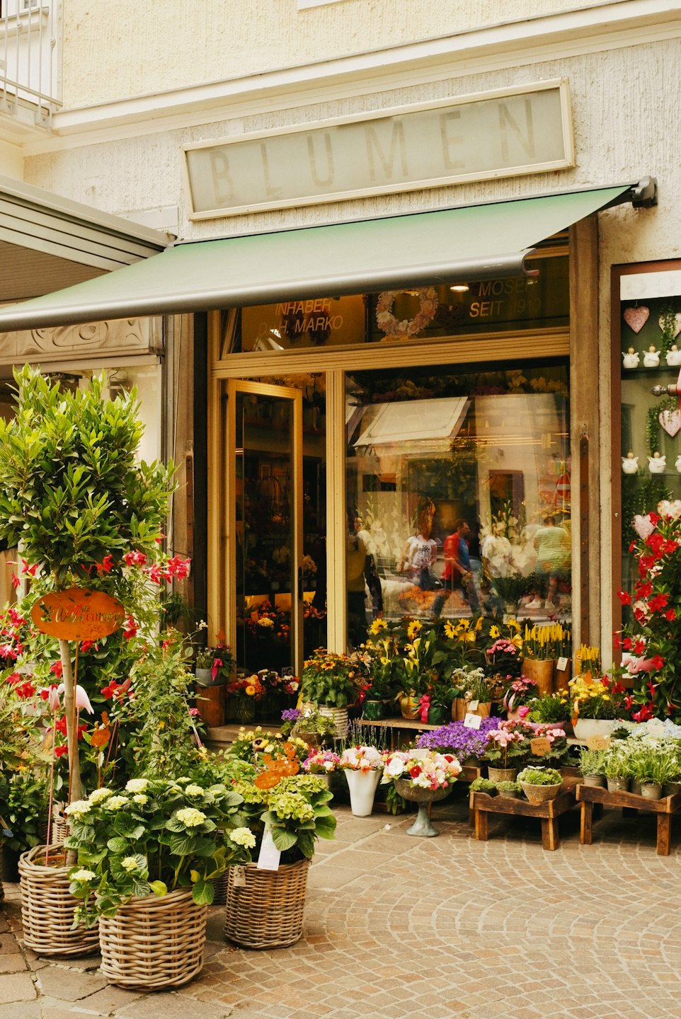 Europeisk blomsterbutik med grönt markis och färgglada växter.