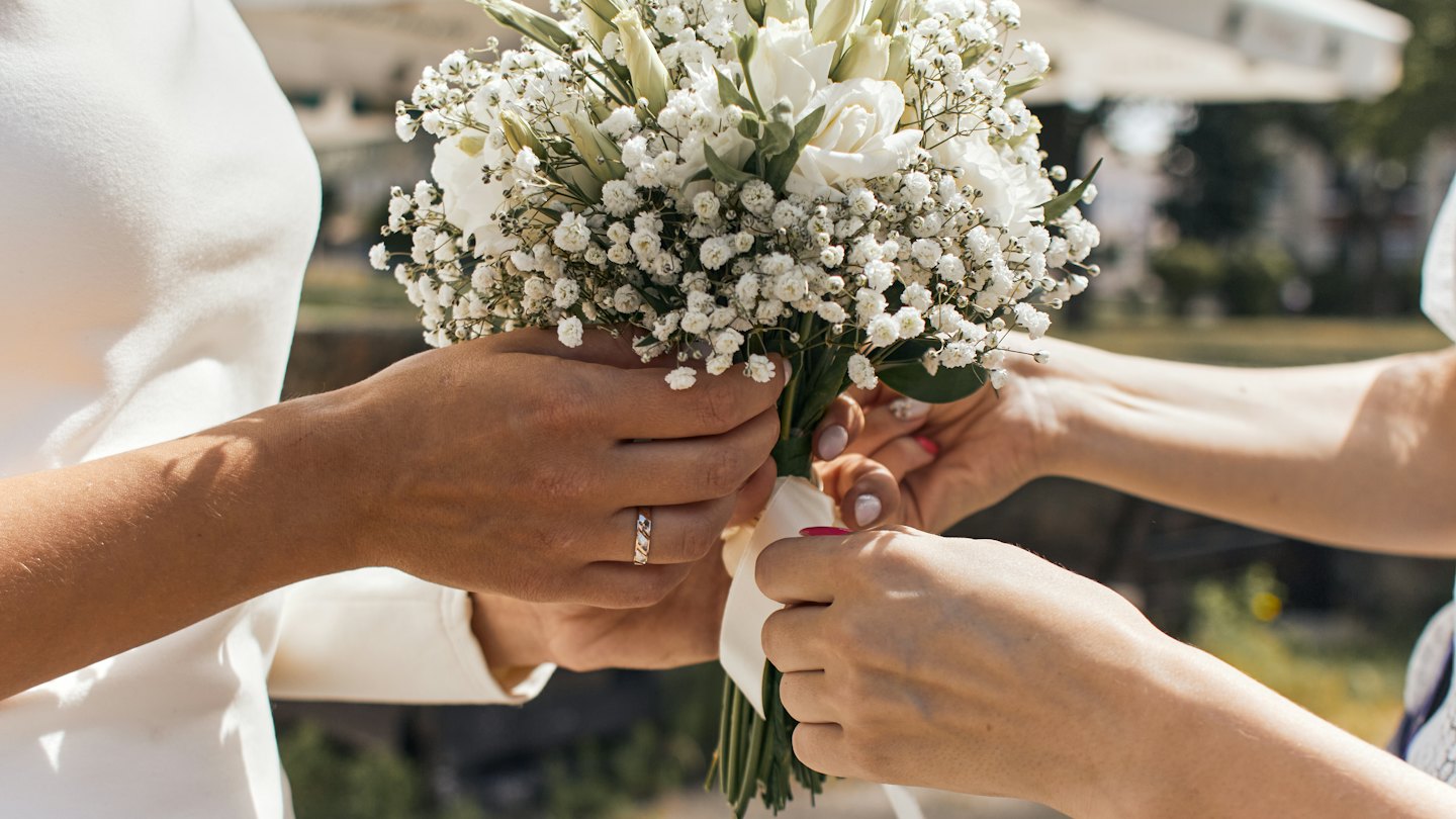 Två personer arrangerar en delikat bukett med vita rosor och blommor.