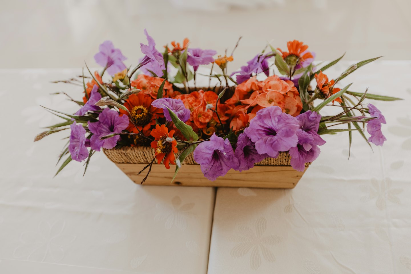 Lila och orange blommor i en trækorg på en duk.