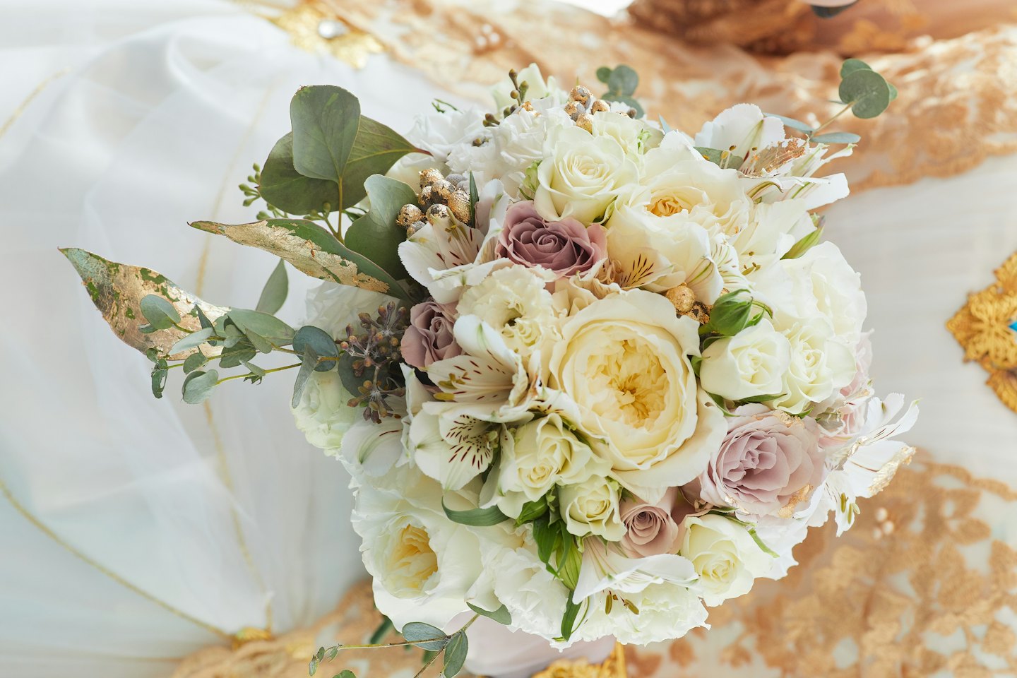 Elegant blomsterbukett med rosor och eukalyptus med gulddetaljer.